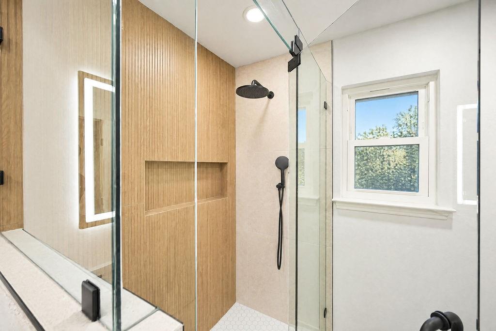 1904 Apollo Road Richardson, TX 75081 - Photo 23 of 40 Glass-enclosed shower with wood-finish wall paneling, built-in shower niche, matte black shower fixtures, and hexagonal floor tiling