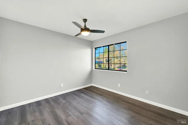 an empty room with wooden floor ceiling fan and windows