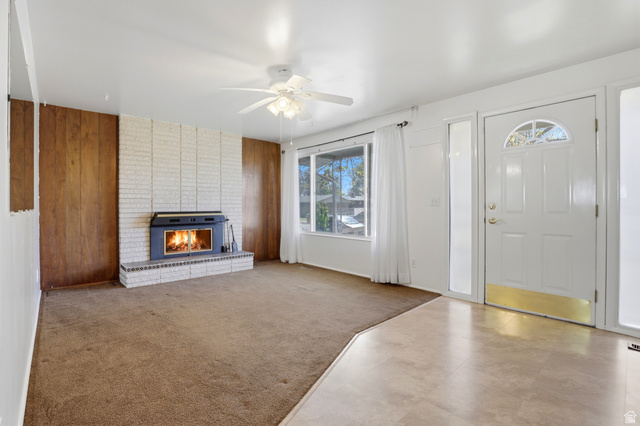 2348 North 770 West Clinton, UT 84015 - Photo 3 of 25 Living area featuring a brick fireplace with an insert, wood paneling, a ceiling fan, and a front entry door with a sidelight