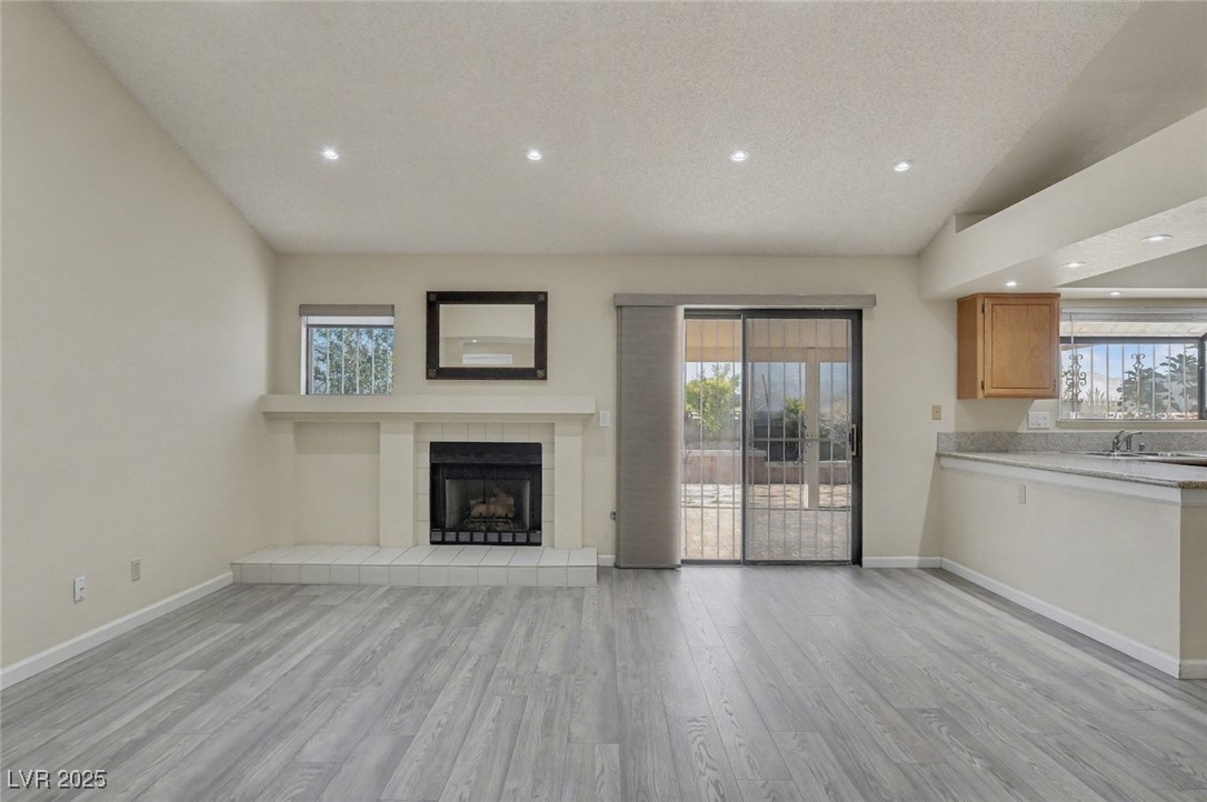 7951 Aspendale Drive Las Vegas, NV 89123 - Photo 11 of 42 Unfurnished living room featuring light wood finished floors, vaulted ceiling, recessed lighting, a fireplace, and a textured ceiling
