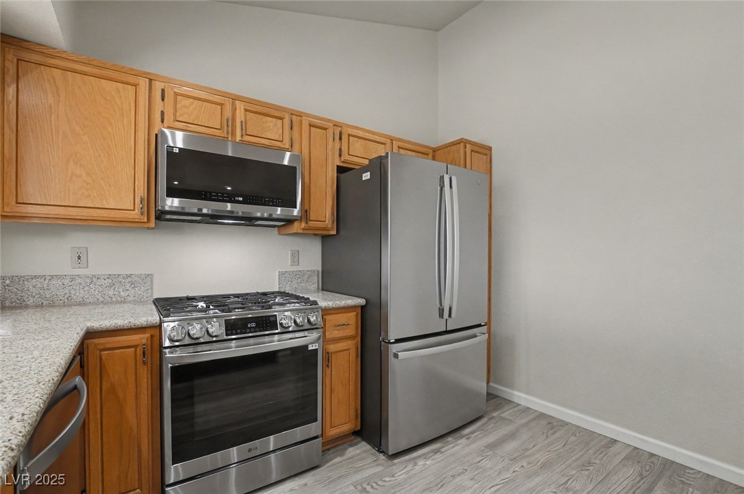 7951 Aspendale Drive Las Vegas, NV 89123 - Photo 15 of 42 Kitchen featuring appliances with stainless steel finishes, light stone countertops, light wood-style flooring, and brown cabinetry