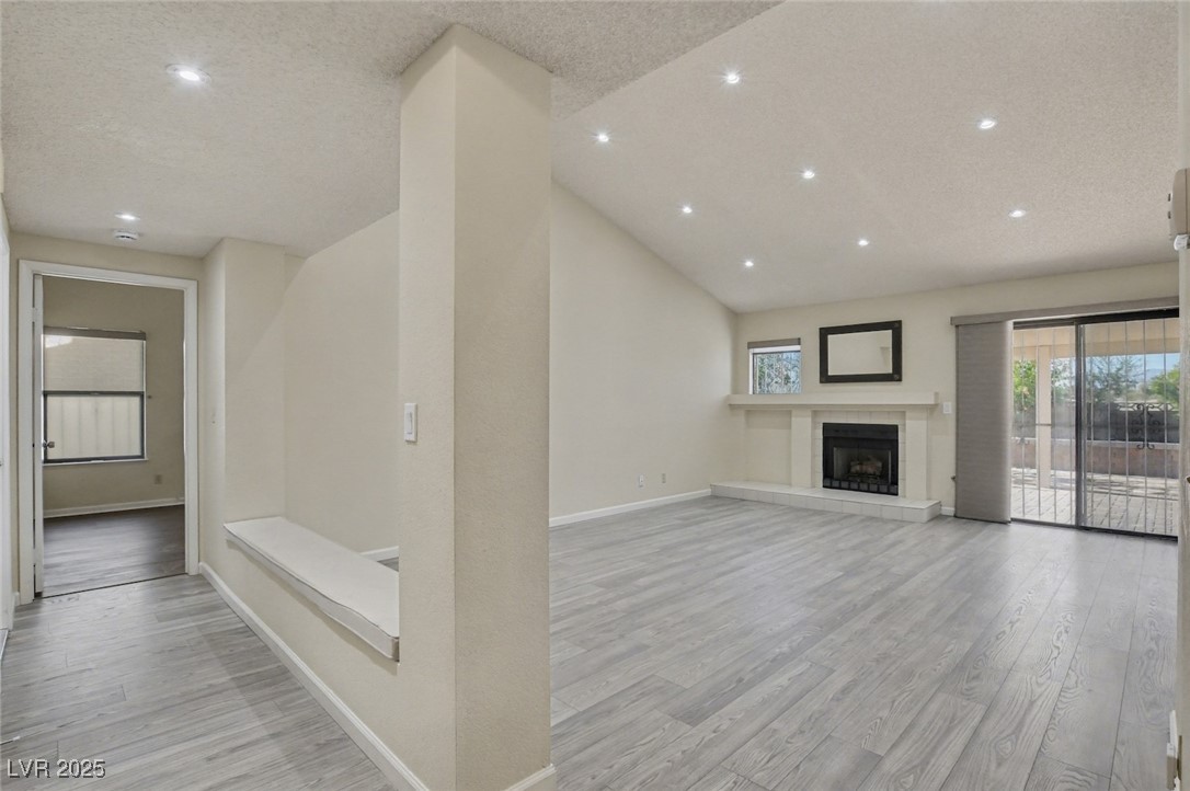 7951 Aspendale Drive Las Vegas, NV 89123 - Photo 19 of 42 Unfurnished living room with lofted ceiling, light wood-type flooring, a tile fireplace, a textured ceiling, and recessed lighting