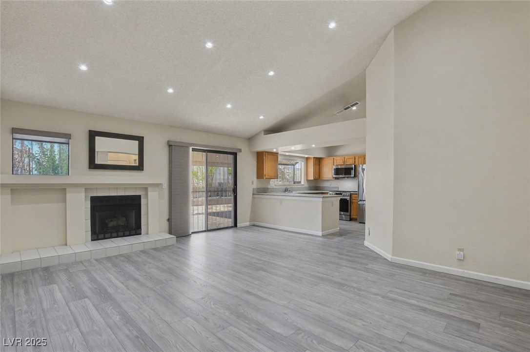 7951 Aspendale Drive Las Vegas, NV 89123 - Photo 5 of 42 Unfurnished living room with light wood-style floors, a tiled fireplace, recessed lighting, and high vaulted ceiling