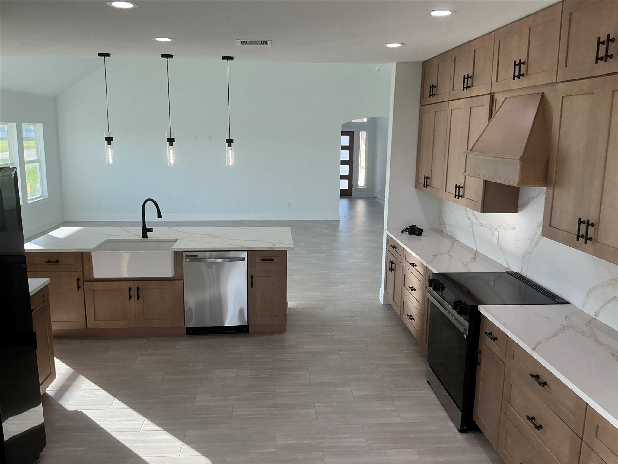471 Buffalo Trail Angleton, TX 77515 - Photo 11 of 35 This photo shows a modern kitchen with light wood cabinetry, quartz countertops, and a central island with a farmhouse sink. It features stainless steel appliances, pendant lighting, and an open layout leading to a bright living area.
