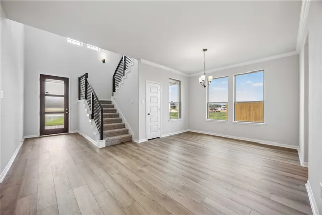 an empty room with wooden floor staircase and windows