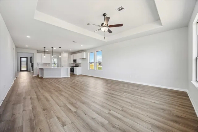 a view of an empty room and kitchen with wooden floor