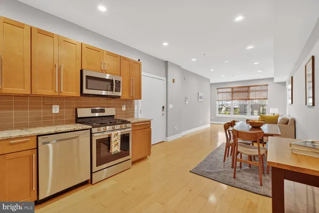 a kitchen with stainless steel appliances granite countertop a stove top oven a sink dishwasher a dining table and chairs with wooden floor