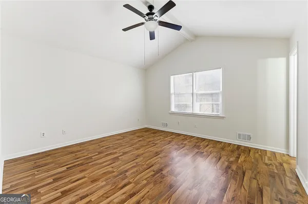 an empty room with wooden floor ceiling fan and windows