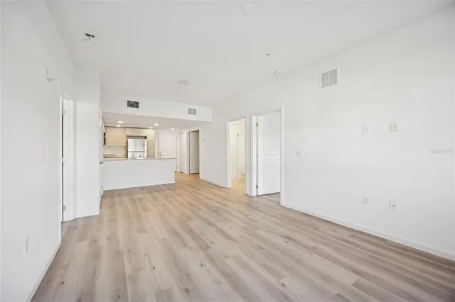 a view of an empty room with wooden floor and kitchen