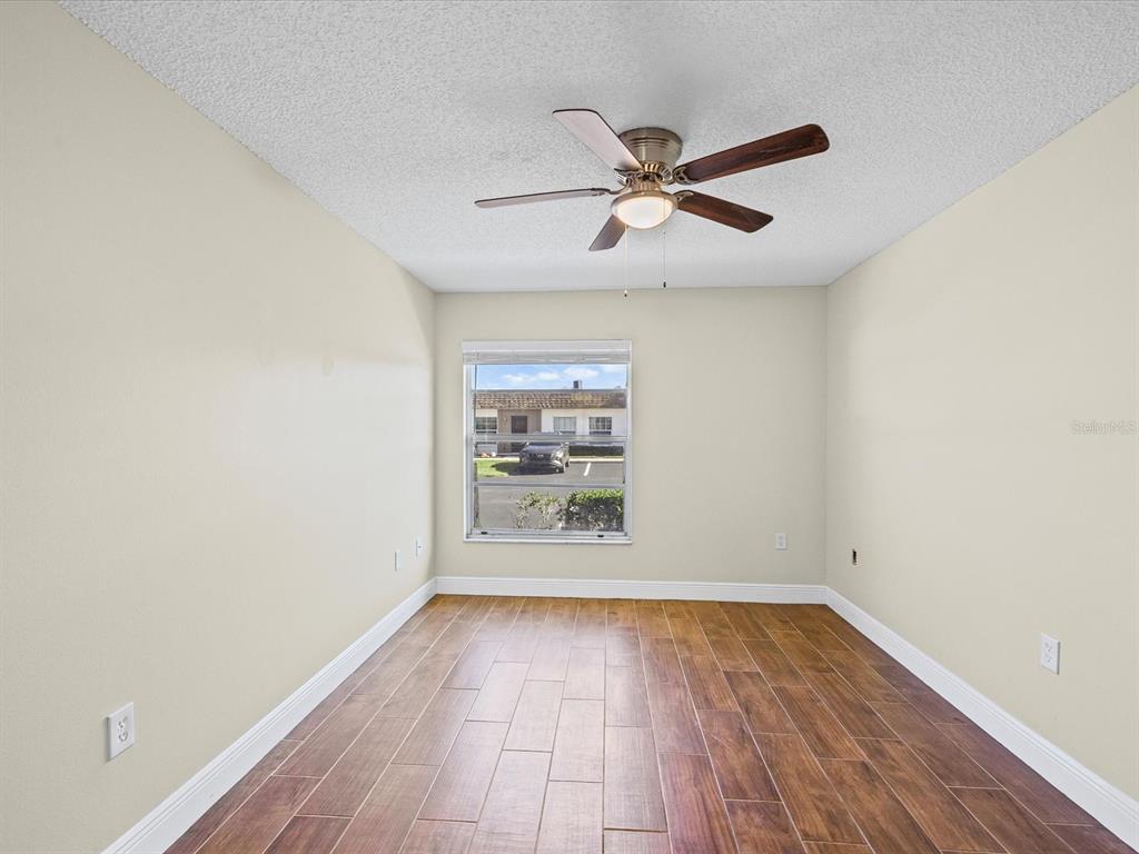 6037 Chesham Drive, Unit 7 New Port Richey, FL 34653 - Photo 22 of 29 an empty room with wooden floor fan and windows