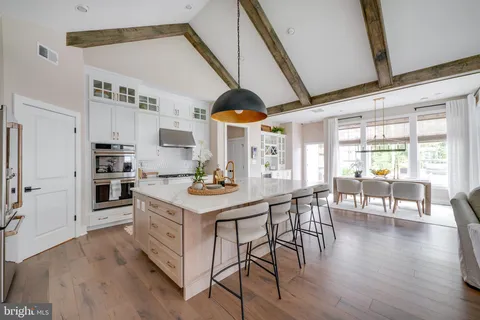 a kitchen with stainless steel appliances kitchen island granite countertop a stove a refrigerator a dining table and chairs with wooden floor