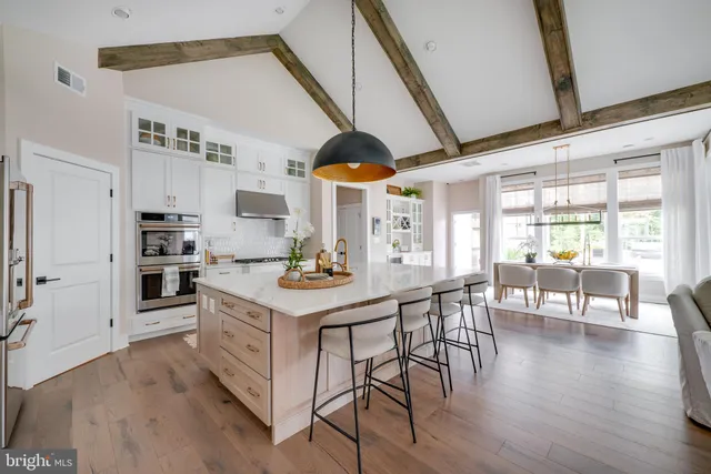 a kitchen with stainless steel appliances kitchen island granite countertop a stove a refrigerator a dining table and chairs with wooden floor