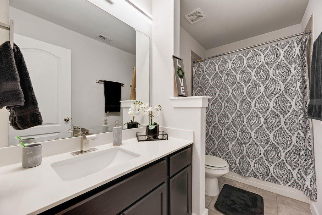 2702 Runnels Court Forney, TX 75126 - Photo 22 of 32 This bathroom features a contemporary vanity with a white countertop and dark cabinetry, a spacious mirror, and a shower area with a patterned curtain