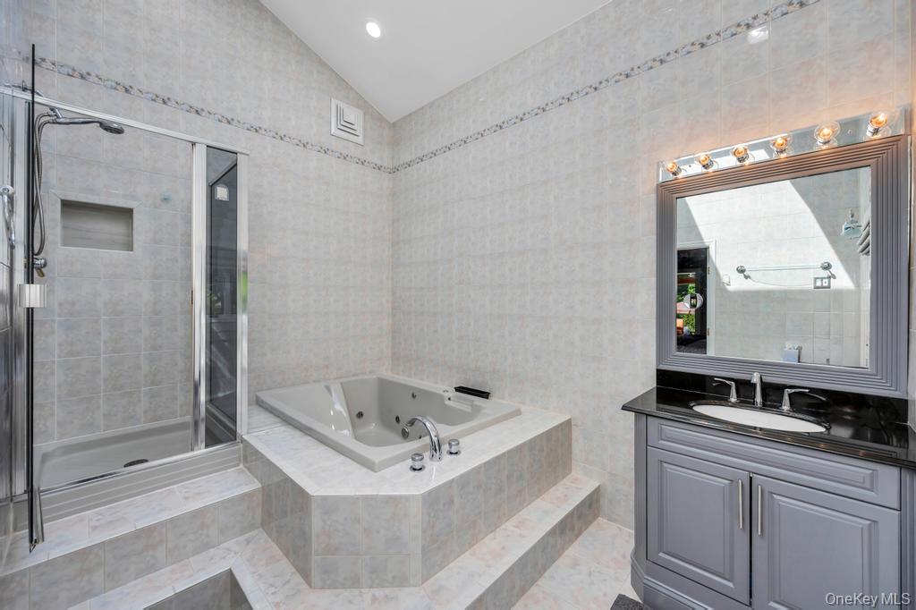 10 South Lot Road Smithtown, NY 11787 - Photo 28 of 50 Bathroom featuring a shower enclosure with a built-in niche, a built-in tub, a vanity with a dark countertop and undermount sink, a framed mirror, and integrated vanity lighting