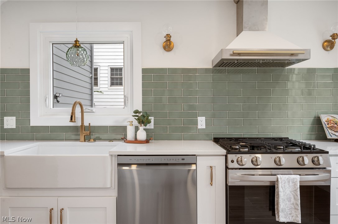 22625 Rye Road Shaker Heights, OH 44122 - Photo 14 of 38 Kitchen featuring a white farmhouse sink with a brass faucet, stainless steel appliances, light green subway tile backsplash, and white cabinetry