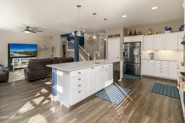 a kitchen with stainless steel appliances kitchen island granite countertop a refrigerator oven a sink dishwasher and white cabinets with wooden floor