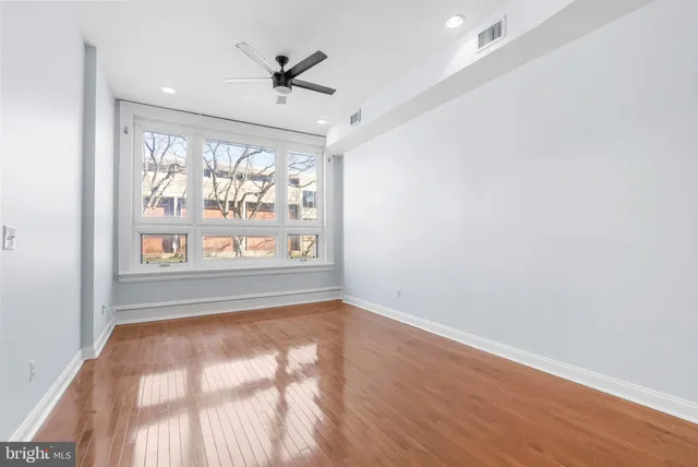 an empty room with wooden floor fan and windows