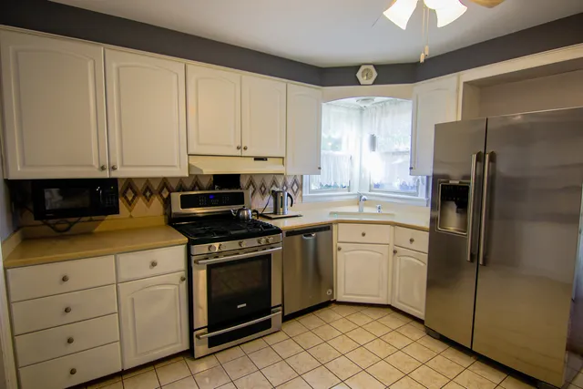 a kitchen with stainless steel appliances granite countertop white cabinets a refrigerator a sink a stove and a window