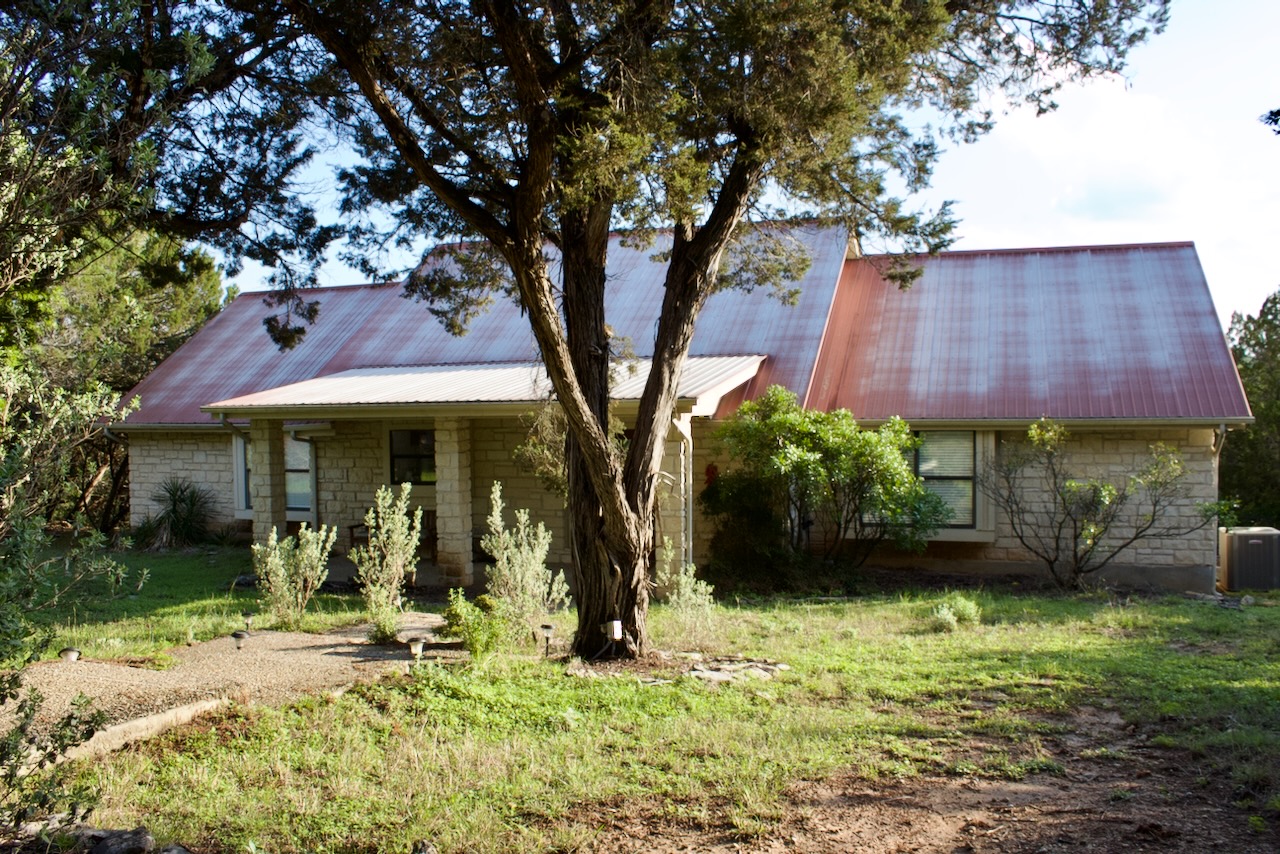 Stone facade residence featuring a covered front porch, red metal roof, and an established tree
