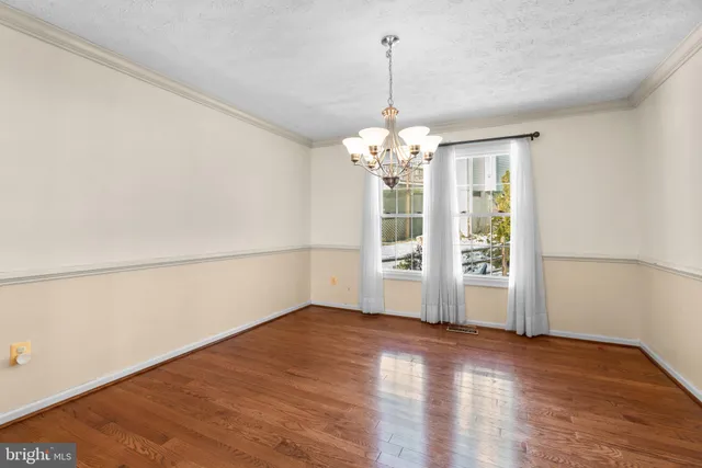 a view of empty room with wooden floor and chandelier