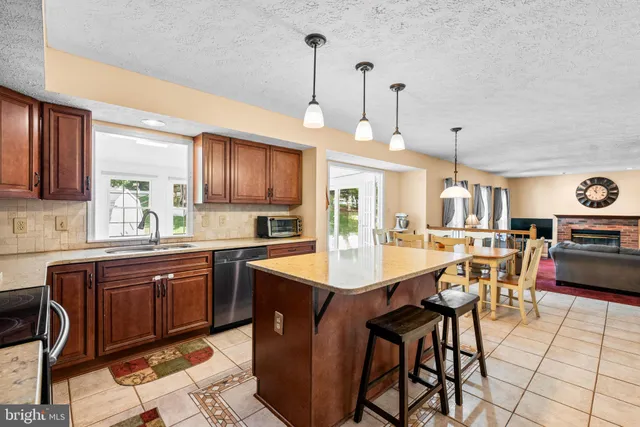 a kitchen with stainless steel appliances granite countertop a stove top oven a refrigerator a sink a dining table and chairs with the cabinets