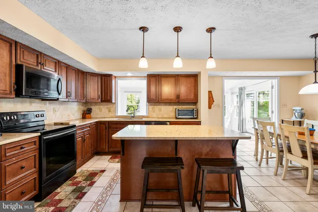 a kitchen with stainless steel appliances granite countertop a stove top oven a refrigerator a sink a dining table and chairs with the cabinets