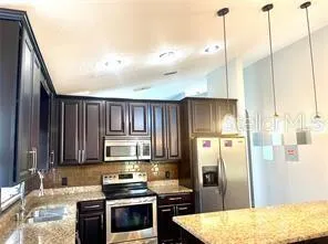a kitchen with kitchen island granite countertop a refrigerator a stove and a sink with wooden floor