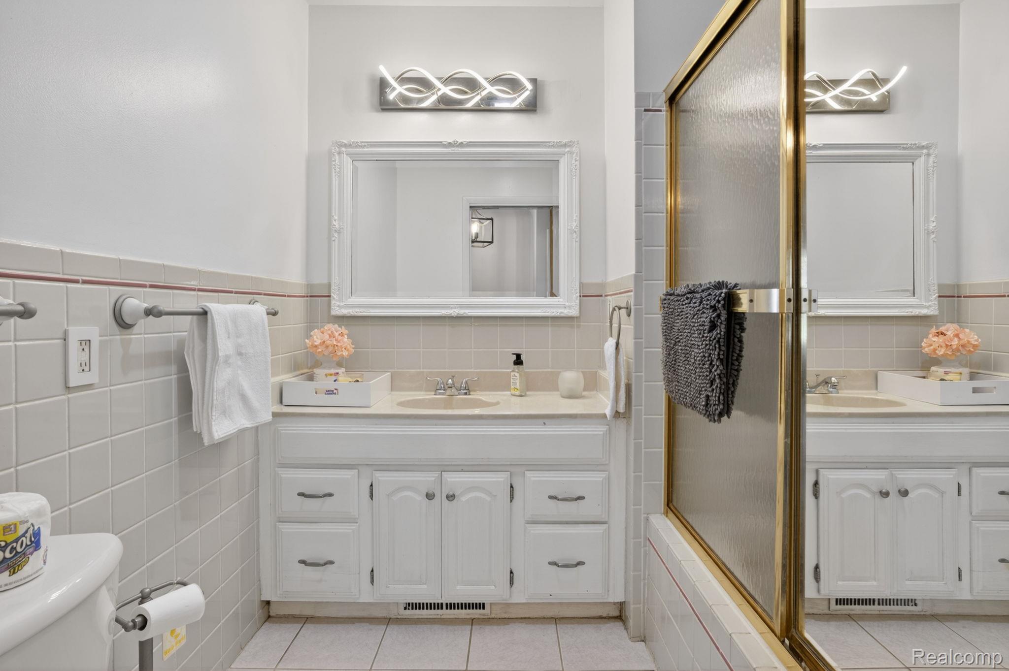 1209 Beatrice Street Flushing, MI 48433 - Photo 20 of 39 Bathroom with two vanities, tile walls, wainscoting, a shower with shower door, and light tile patterned floors