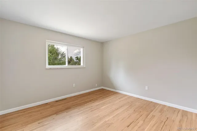 a view of an empty room with a window and wooden floor