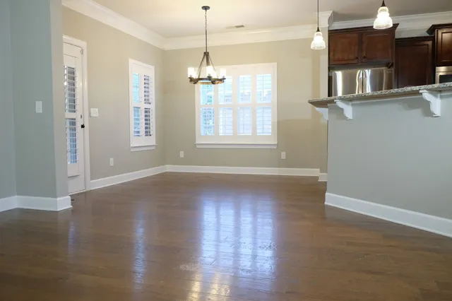 an empty room with wooden floor chandelier and windows