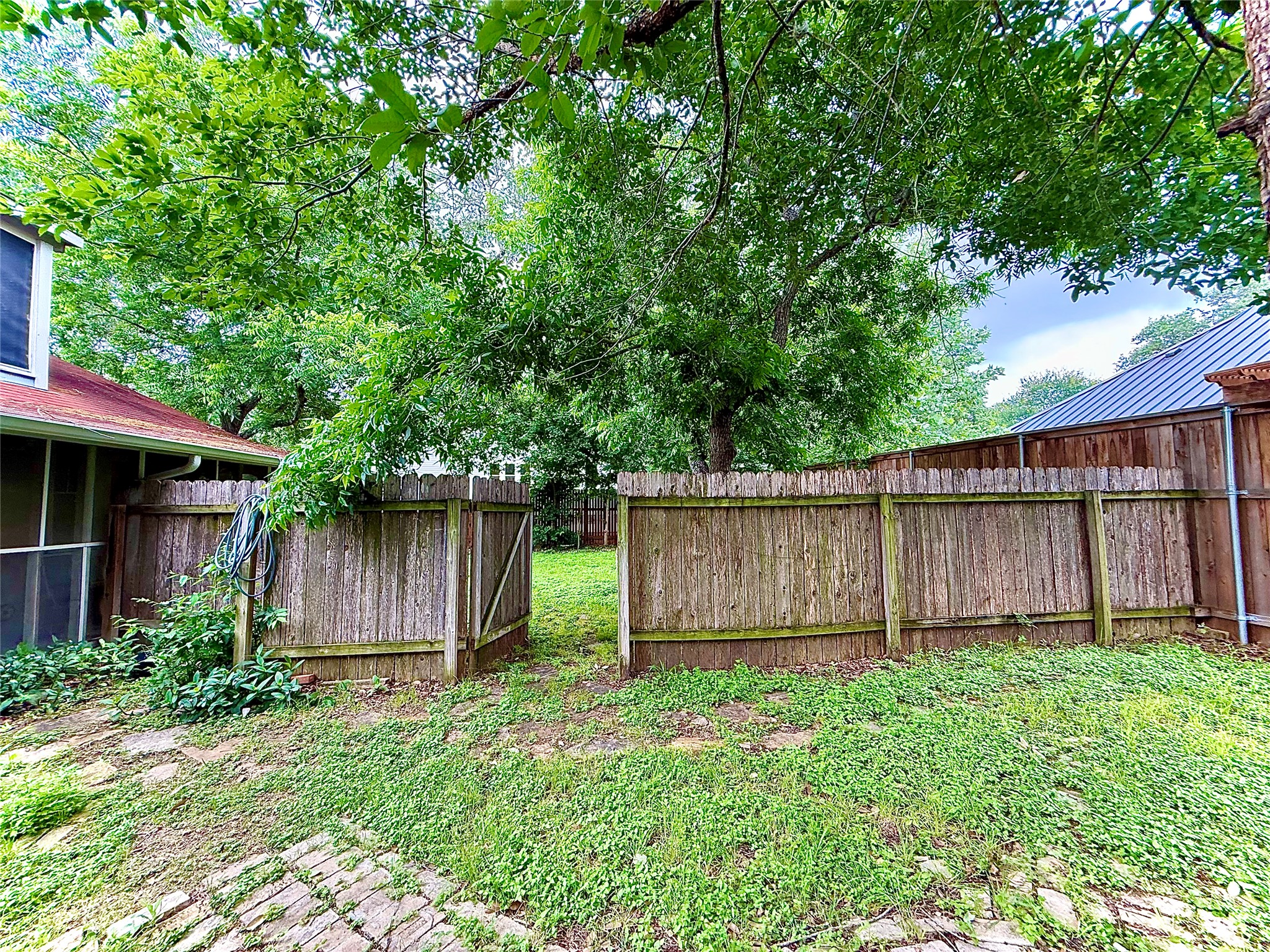 423 South Main Street Lockhart, TX 78644 - Photo 25 of 26 Private backyard with a wood privacy fence and gate, partially brick-paved patio, and mature trees providing natural shade