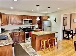 26 Bacon Street, Unit 26 Watertown, MA 02472 - Photo 2 of 12 a kitchen with stainless steel appliances granite countertop a stove top oven a sink a dining table and chairs with wooden floor