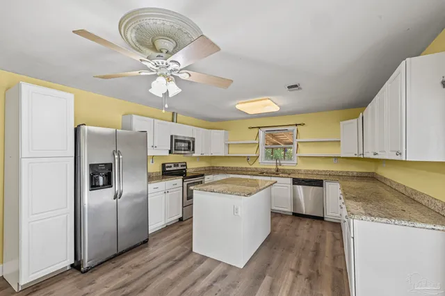 a kitchen with stainless steel appliances granite countertop a refrigerator a sink dishwasher a stove and white countertops with wooden floor