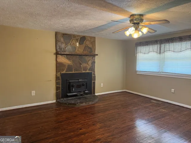 a view of an empty room with wooden floor fireplace and a window