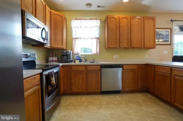 a kitchen with stainless steel appliances granite countertop a sink a stove a refrigerator cabinets and a window