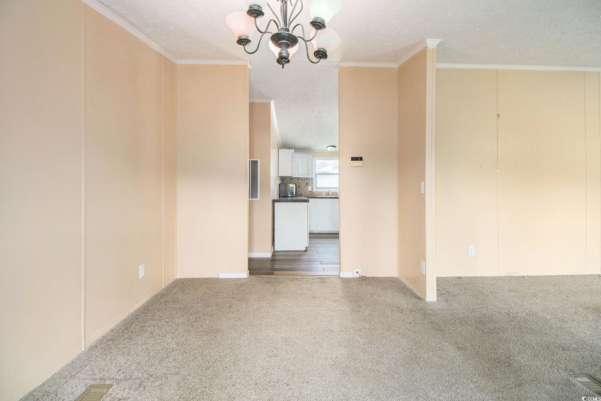 3804 Stern Drive Conway, SC 29526 - Photo 12 of 38 Empty room featuring a textured ceiling, dark colored carpet, a chandelier, and ornamental molding