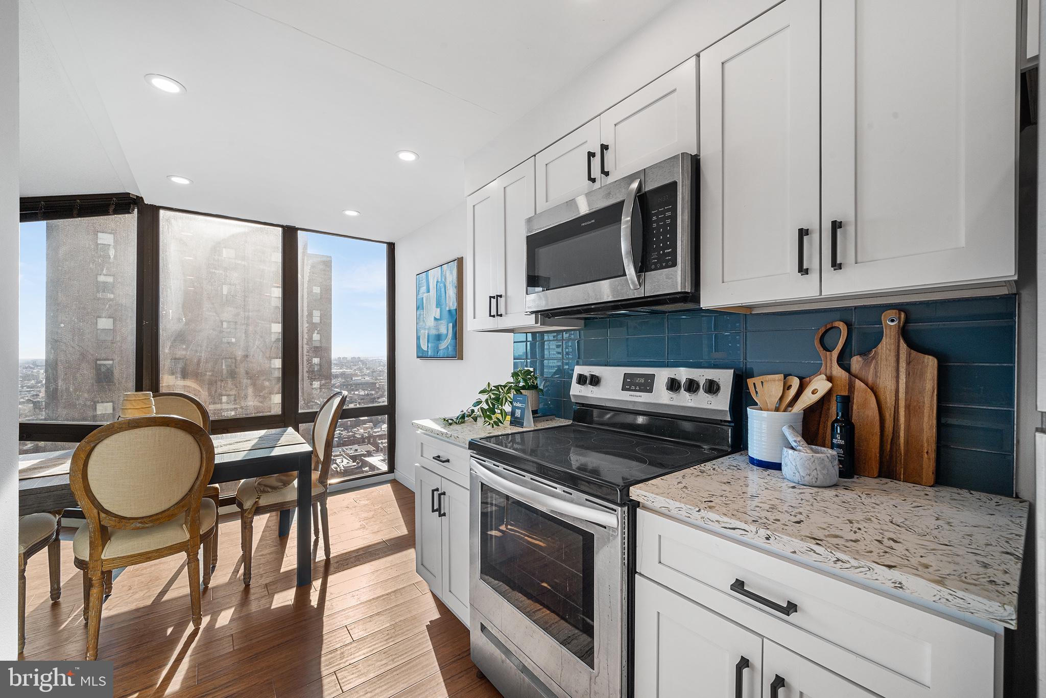 2018 Walnut Street, Unit 16E Philadelphia, PA 19103 - Photo 13 of 35 a kitchen with stainless steel appliances granite countertop a stove a sink a microwave a refrigerator white cabinets and a dining table with wooden floor