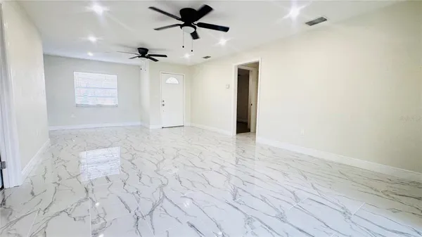 an empty room with wooden floor chandelier fan and windows