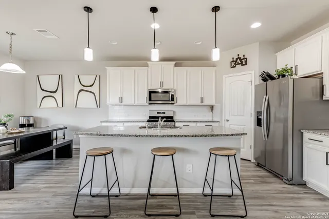 a kitchen with stainless steel appliances granite countertop a kitchen island a stove a refrigerator a sink a dining table and chairs with wooden floor