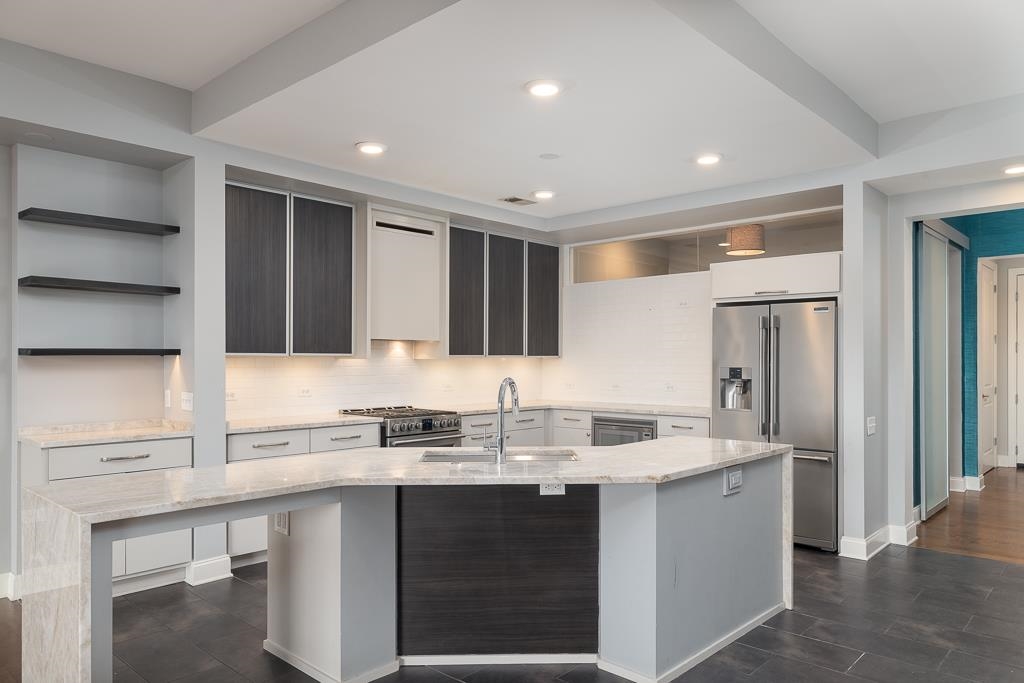 717 Riverside Drive, Unit 1105 Memphis, TN 38103 - Photo 4 of 29 Kitchen featuring light stone counters, backsplash, premium appliances, open shelves, and an island with sink