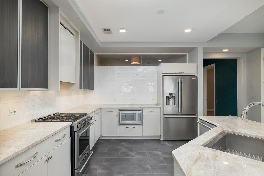 717 Riverside Drive, Unit 1105 Memphis, TN 38103 - Photo 5 of 29 Kitchen featuring appliances with stainless steel finishes, light stone counters, backsplash, white cabinets, and recessed lighting