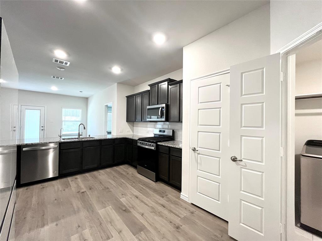 758 Musket Street Fate, TX 75189 - Photo 11 of 26 Kitchen with appliances with stainless steel finishes, light stone counters, light wood finished floors, dark cabinetry, and recessed lighting