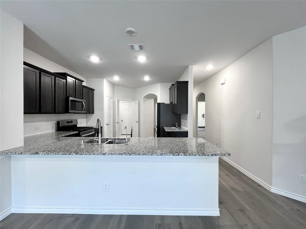 758 Musket Street Fate, TX 75189 - Photo 5 of 26 Kitchen featuring arched walkways, light stone countertops, dark wood finished floors, stainless steel appliances, and a peninsula