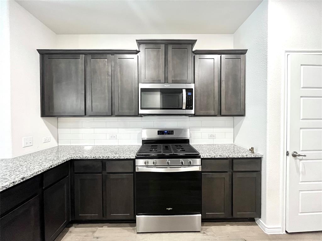 758 Musket Street Fate, TX 75189 - Photo 6 of 26 Kitchen featuring stainless steel appliances, backsplash, light stone counters, and light wood-style floors