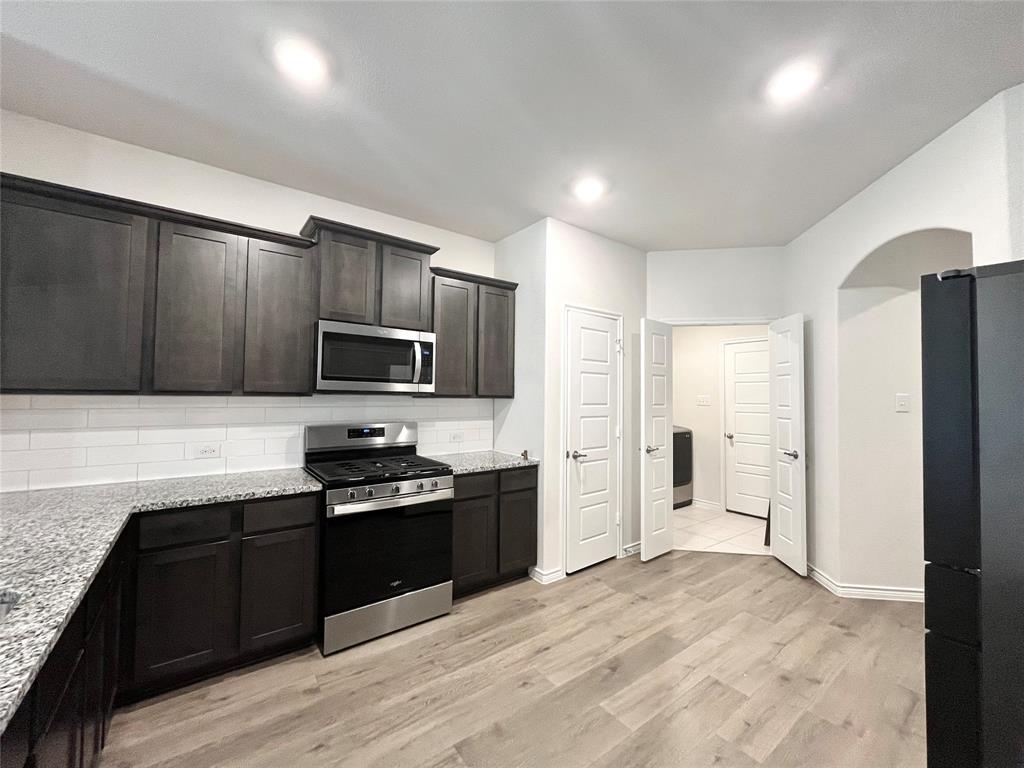 758 Musket Street Fate, TX 75189 - Photo 9 of 26 Kitchen with stainless steel appliances, decorative backsplash, light stone counters, light wood-style flooring, and arched walkways