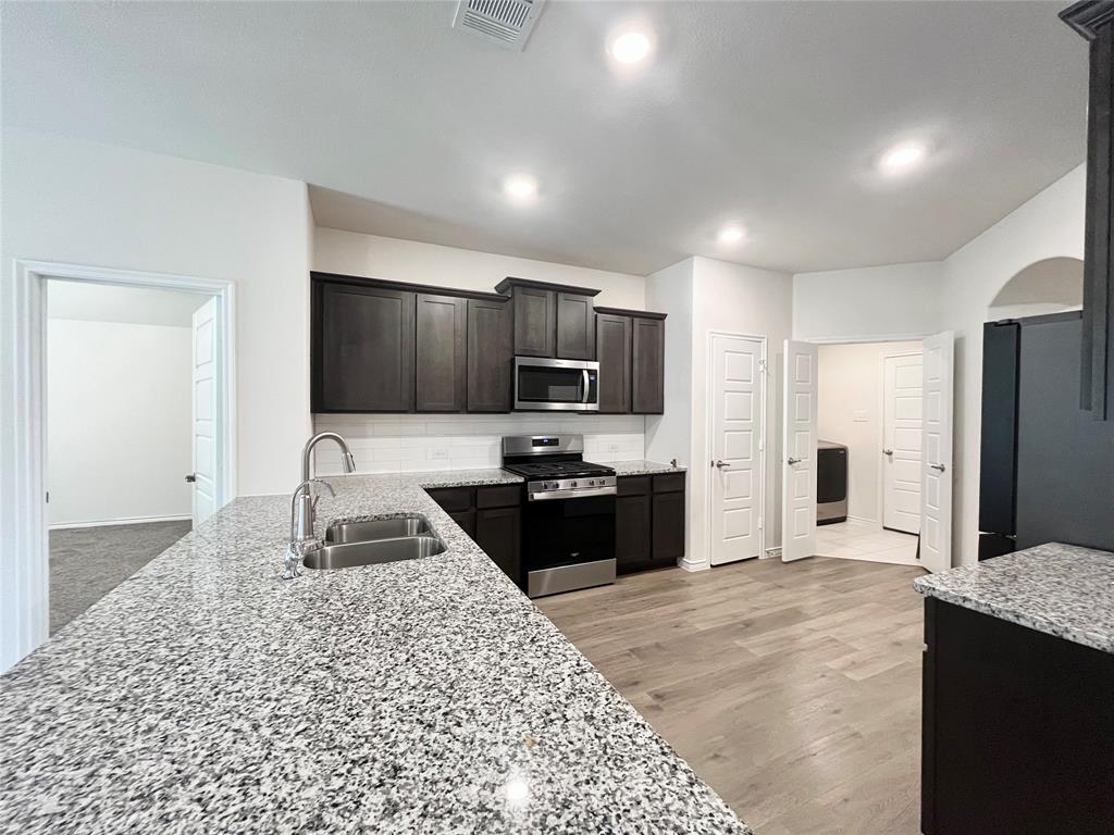 758 Musket Street Fate, TX 75189 - Photo 10 of 26 Kitchen featuring stainless steel appliances, light stone counters, recessed lighting, dark brown cabinets, and light wood-style flooring