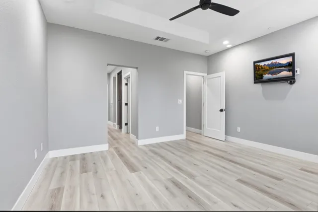 a view of an empty room with wooden floor and a ceiling fan