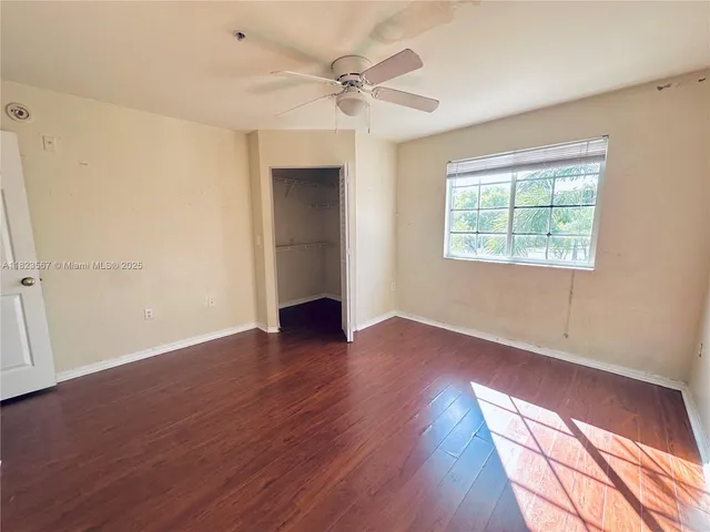 an empty room with wooden floor fan and windows