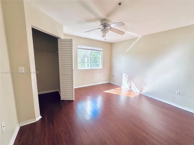 an empty room with wooden floor fan and windows
