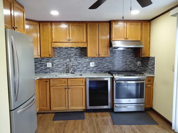 a kitchen with stainless steel appliances kitchen island granite countertop a refrigerator a sink and wooden cabinets